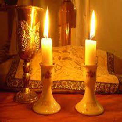 Shabbat candles in front of a kiddish cup and covered chalah bread.